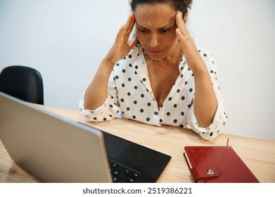 A frustrated woman experiencing stress while working on her laptop, demonstrating workplace challenges and pressure in a modern office environment. - Powered by Shutterstock