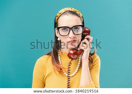 Frustrated woman having a boring phone call, she is holding the receiver and looking at camera