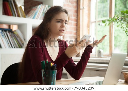 Frustrated woman having problem with not working smart phone sitting at home office desk, indignant confused businesswoman annoyed with discharged or broken cell, received bad news in mobile message