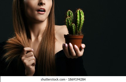Frustrated woman with long silky straight hair in black body holding cactus plant in pot and comparing with split ends over dark background, cropped composition. Haircare, beauty, wellness concept