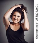 Frustrated, woman and pulling hair in studio portrait for anger, rage and mental health with stress. Bipolar girl, person and moody with anxiety, annoyed and aggressive for crisis on gray background