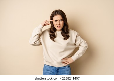 Frustrated Woman Roll Finger Near Head And Complaining, Insulting Someone, Standing Over Beige Background