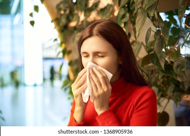 A frustrated woman sneezes due to allergies at the Mall. The concept of spring exacerbation of allergies, runny nose, colds.