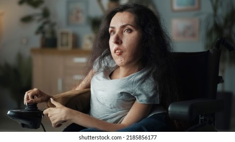 Frustrated woman with spinal muscular atrophy sitting in a wheelchair in a dim living room illuminated by a lamp - Shutterstock ID 2185856177