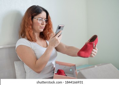 A Frustrated Woman Unpacks An Online Purchase And Takes A Photograph Of The Shoe On A Smartphone. The Girl Received The Wrong Package