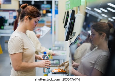 A frustrated woman uses a self-checkout counter. The girl does not understand how to independently buy groceries in the supermarket without a seller