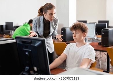 Frustrated worried young female teacher emotionally talking to neglectful teenage student sitting at computer in classroom during lesson - Powered by Shutterstock