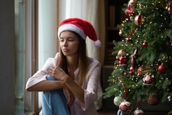 Frustrated Xmas Young Woman Getting Bored At Christmas Tree, Sitting At Window At Home, Thinking Over Problems, Feeling Lonely, Sad, Depressed, Suffering From Apathy, Loneliness On Holiday Time
