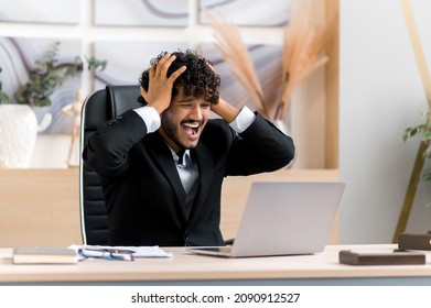 Frustrated Young Adult Ceo, Businessman Or Manager From India, With A Beard, Sitting At A Table In The Office, Frustrated With Financial Losses, Collapse, Stressed With Hand Gestures, Shouts