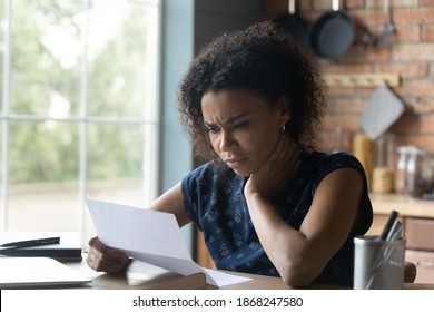 Frustrated young african american woman reading paper letter with bad news, stressed of getting bank debt or loan rejection notification, feeling confused of termination notice, sitting at table. - Shutterstock ID 1868247580