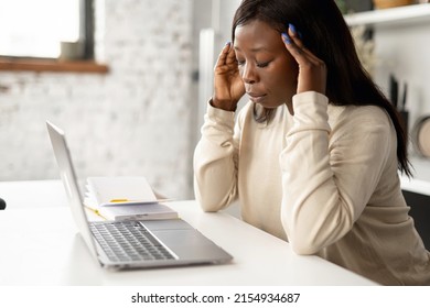 Frustrated Young African American Woman Using Laptop Computer Suffering From Headache, Sitting In Home Office And Holding Head With Hands, Feels Sick And Unwell, Burnout And Overworked