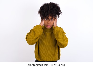 Frustrated Young beautiful African American woman wearing knitted sweater against white wall,  plugging ears with hands does not wanting to listen hard rock, noise or loud music. - Shutterstock ID 1876450783