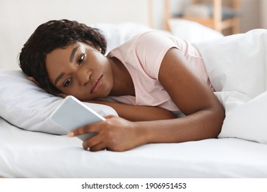 Frustrated Young Black Woman Looking At Smartphone Screen While Laying In Bed Before Sleeping, Feeling Lonely Or Depressed, Closeup. Upset African American Lady Waiting For Call From Lover