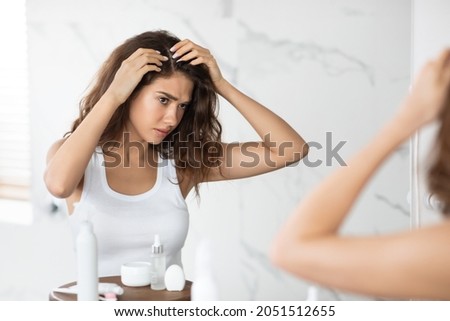 Frustrated Young Lady Searching Hair Flakes Suffering From Dandruff Problem Standing Near Mirror In Bathroom Indoors. Haircare And Head Skin Health Concept. Selective Focus Foto stock © 