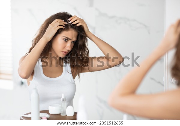 Frustrated Young Lady
Searching Hair Flakes Suffering From Dandruff Problem Standing Near
Mirror In Bathroom Indoors. Haircare And Head Skin Health Concept.
Selective Focus