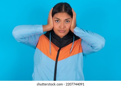 Frustrated Young Latin Woman Wearing Sport Clothes Over Blue Background Plugging Ears With Hands Does Not Wanting To Listen Hard Rock, Noise Or Loud Music.