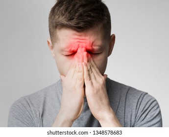 Frustrated young man suffering from sinus pressure, touching his nose with closed eyes