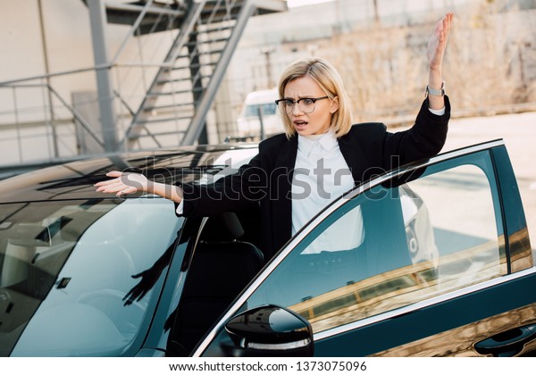 frustrated young woman gesturing near black car in\
parking 