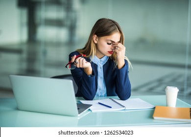 Frustrated young woman keeping eyes closed and massaging nose while sitting at her working place in office