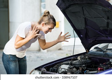 Frustrated Young Woman Looking At Broken Down Car Engine On Street