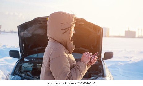 Frustrated young woman with phone waits for tow truck near broken automobile with open bonnet on road among snowy fields in cold winter, sunlight - Powered by Shutterstock