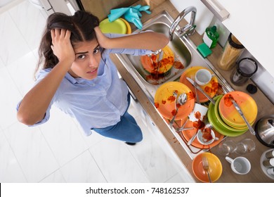 Frustrated Young Woman Standing Near Messy Utensils On Countertop In Kitchen