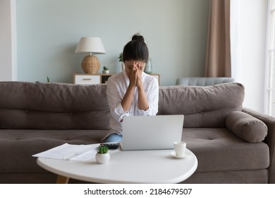 Frustrated Young Woman Touching Face With Closed Eyes Over Heap Of Paper Bills, Documents, Calculator, Sitting On Couch At Laptop Computer, Thinking Over Overspending, Bankruptcy