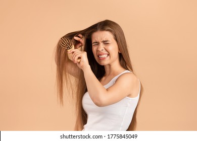 Frustrated young woman trying to brush her tangled long hair against beige background - Powered by Shutterstock