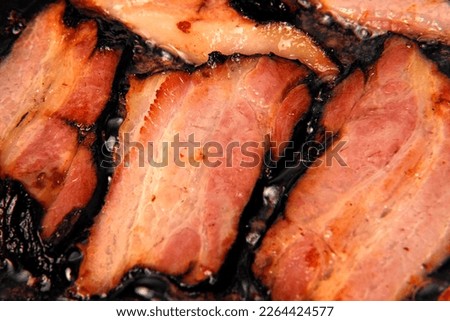 Frying Bacon Slices in a Pan. Crispy Pieces of Delicious Red Thin Smokey Bacon Fried in a Hot Skillet. Traditional Breakfast. Smoked Bacon Rasher or Strip Being Cooked. Grill. Fat High Calorie Food.