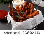 Frying basket with sweet potato fries and sauces on black table, closeup