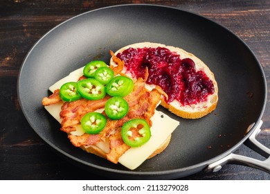 Frying A Blackberry Bacon Grilled Cheese Sandwich In A Skillet: Two Halves Of A Grilled Cheese Sandwich With Bacon In A Nonstick Frying Pan