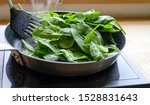 frying fresh spinach in a pan on the stove, healthy cooking at home concept, selected focus, narrow depth of field
