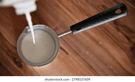 A frying pan with batter inside on a wooden kitchen counter, ready for cooking.