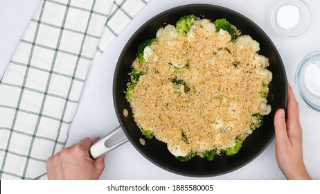 Frying Pan With Cauliflower And Broccoli Topped With Alfredo Sauce And Bread Crumbs Close Up In Woman Hands. Step By Step Vegetable Casserole Recipe, Cooking Process