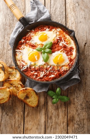 Frying pan with eggs in purgatory closeup on wooden background. Vertical top view from above

