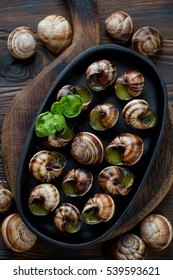 Frying Pan With Escargot Snails On A Rustic Wooden Background, Overhead View