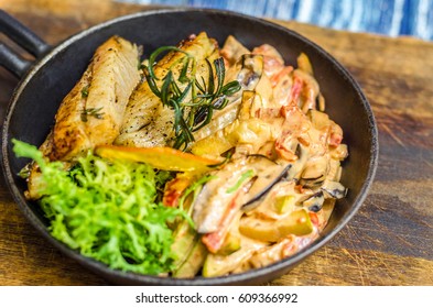 Frying pan with fish, lemon and herbs on a wooden board