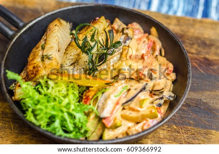 Frying pan with fish, lemon and herbs on a wooden board