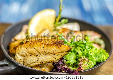 Frying pan with fish, lemon and herbs on a wooden board