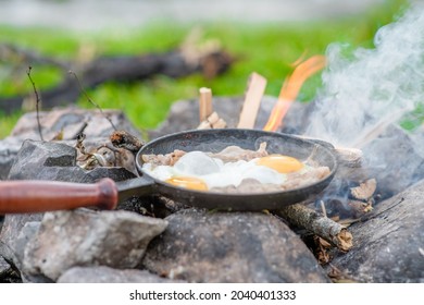 Frying pan with fried eggs and bacon stands on the campfire in nature