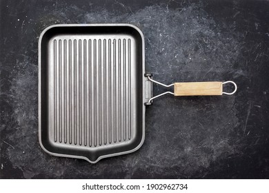 Frying Pan Grill On Black Grunge Background, Top View. Empty Cast Iron Griddle, Overhead View. Square Grill Pan On Black Shabby Table.