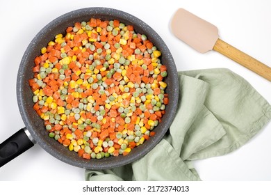 Frying Pan With A Mix Frozen Vegetables: Carrots, Green Peas, Corn Grains On A White Background, Top View. Cooking Frozen Vegetables In A Pan.