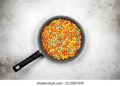 Frying Pan With A Mix Frozen Vegetables: Carrots, Green Peas, Corn Grains On A White Background, Top View. Cooking Frozen Vegetables In A Pan