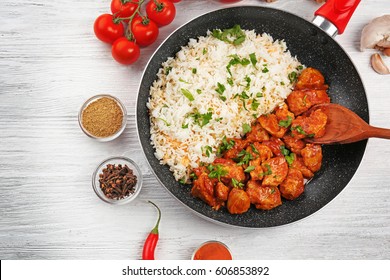 Frying pan with tasty chicken tikka masala and rice on wooden table