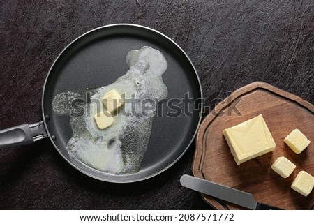 Frying pan and wooden board with fresh butter on dark background