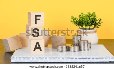FSA - text on a stack of wooden blocks standing on a notepad with coins, a flower in a pot on a yellow background