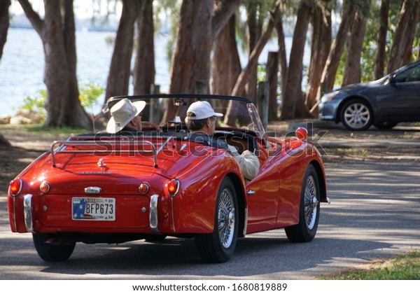 Ft. Myers, Florida/USA - March 1,\
2020: A horizontal image of a red sports car driving into an\
antique car show in southwest Florida.                         \
