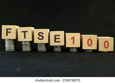 FTSE 100 UK Stock Market Index Crash And Bear Market Due To Financial Crisis And Recession In London UK. Wooden Blocks In With Coins In Dark Black Background.