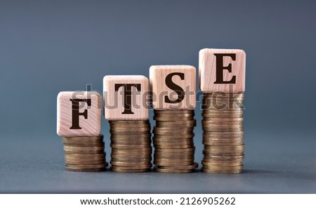 FTSE (Financial Times Stock Exchange Group) - acronym on wooden cubes on coins on a gray background. Business concept