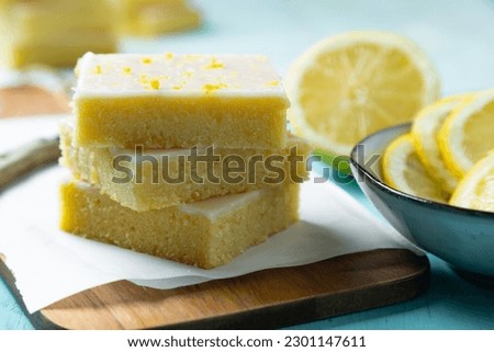  Fudgy lemon brownies with lemon glaze and zest on baking paper on an aquamarine background